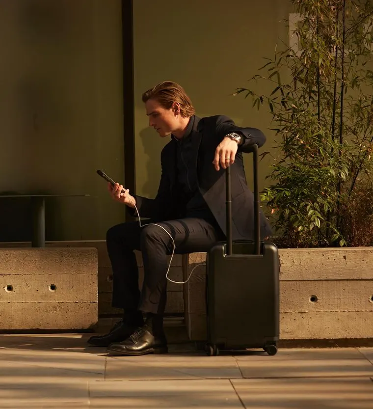 A man checks his phone next to his luggage while his cancelled flight is rebooked