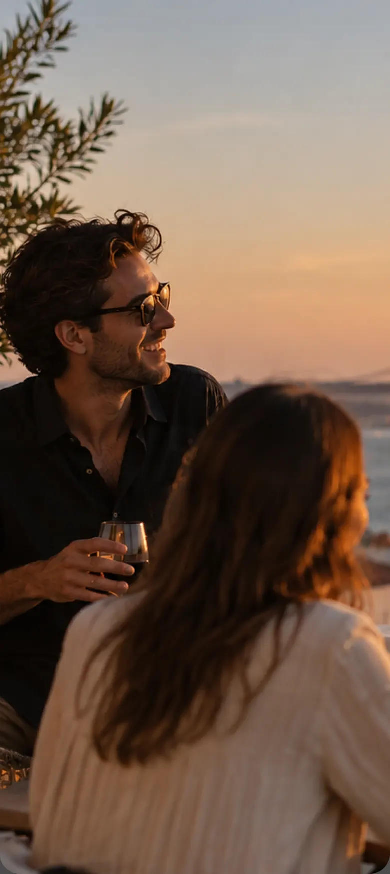 Friends toasting at a rooftop dinner overlooking a sunset and a suspension bridge