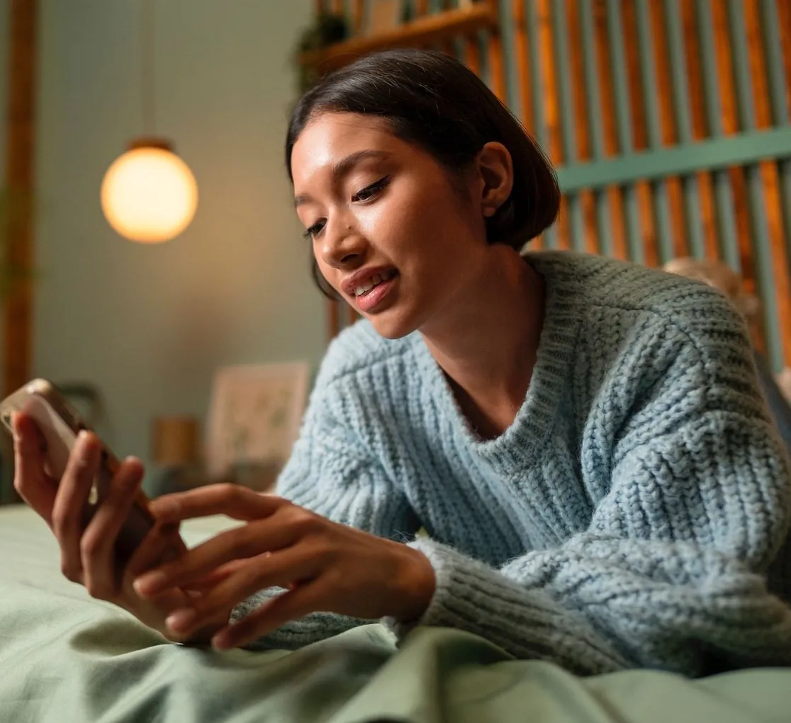 A woman in a knitted sweater lying on a sofa, speaking into her phone