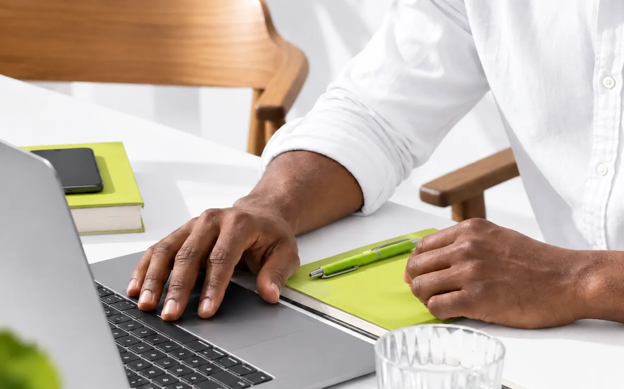 Hands working on a laptop at a bright desk beside a lime-green notebook