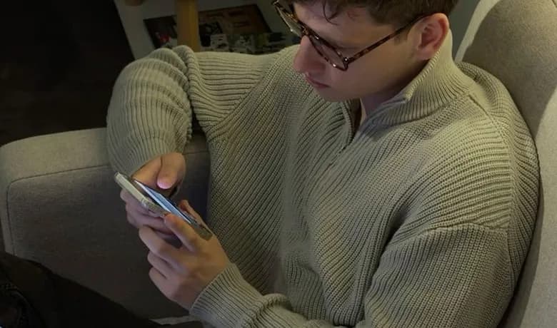 A man in a knitted sweater reading on his phone